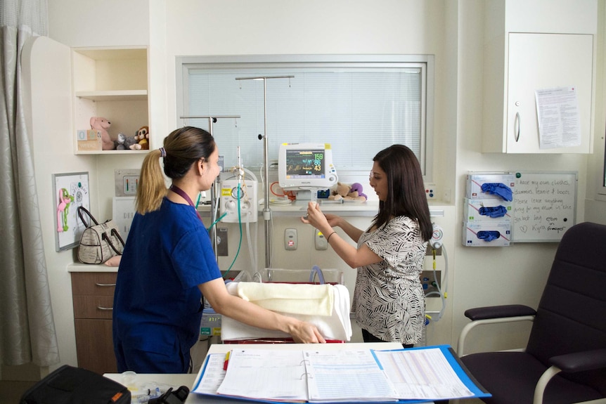 A nurse checks on Kyra as Rachel holds up her feeding tube.