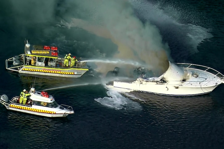 Firefighters on two boats spray hoses towards a cruiser boat on fire.