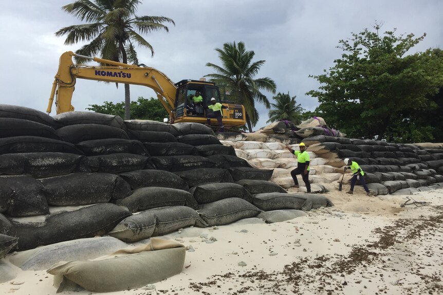 Workers and machinery working on large wall of sand bags. 