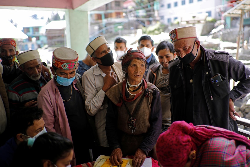 A group of villagers gather together. Most are wearing masks