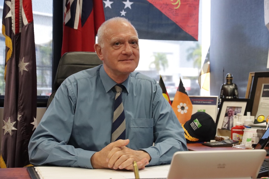 a man in his 60s or 70s sitting in an office wearing a suit