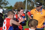 A girl with sweaty brown hair in a ponytail and red and blue jersey takes a drink with her team during a break