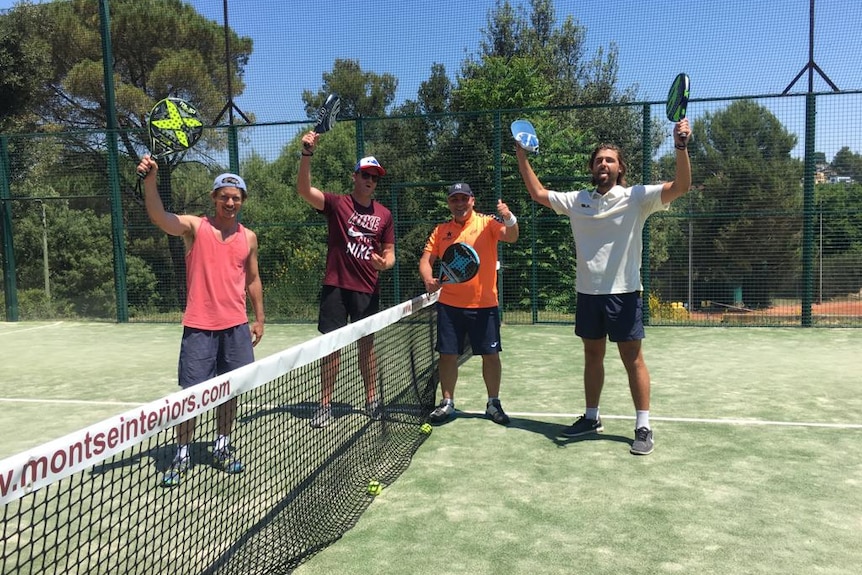 Four players holding rackets next to a net in a tennis court