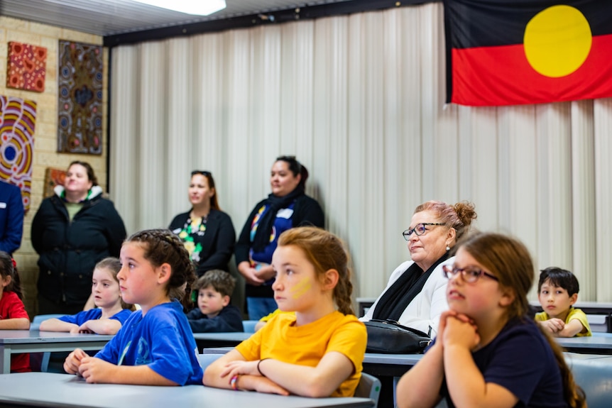 An adult sitting in a classroom with children.