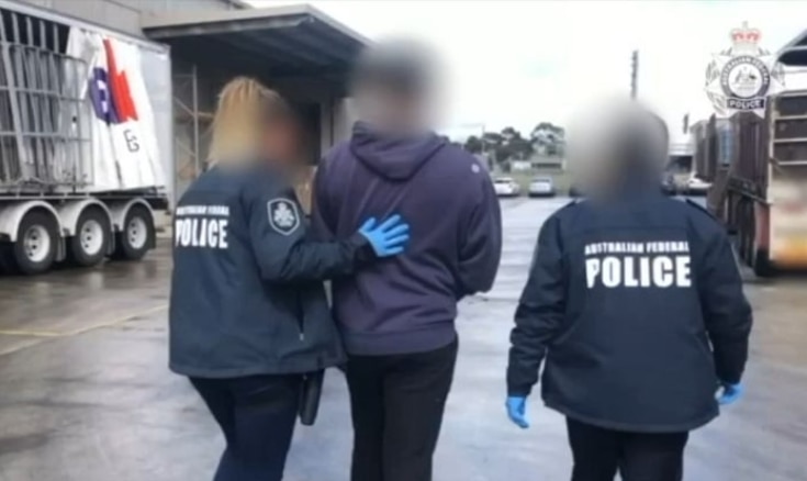 Police lead a man in handcuffs to a car in a carpark.