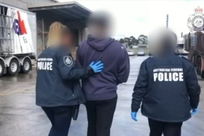 Police lead a man in handcuffs to a car in a carpark.