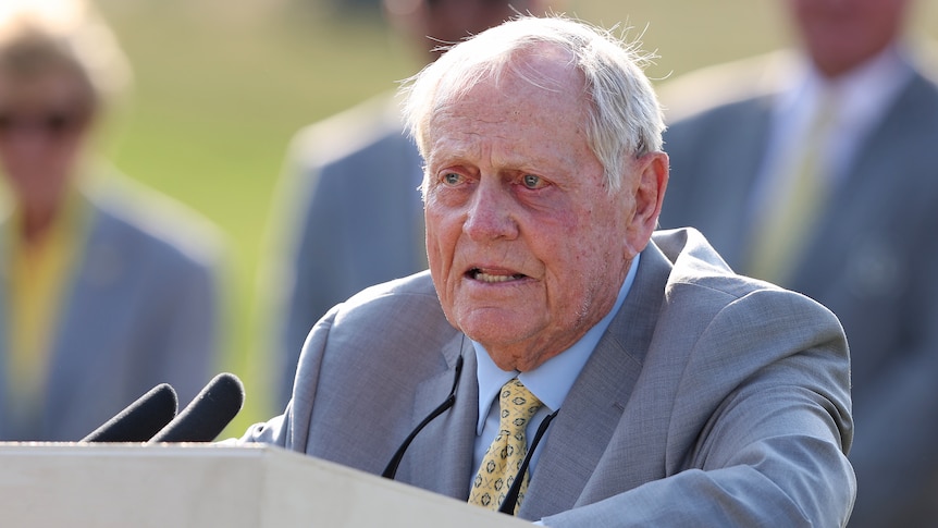 Golfing great Jack Nicklaus stands at a lectern with microphones in front of him.
