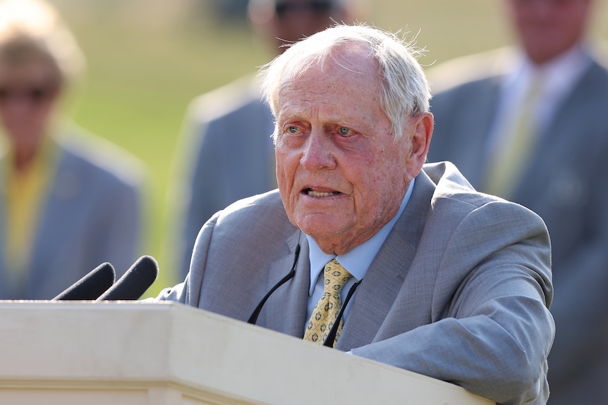 Golfing great Jack Nicklaus stands at a lectern with microphones in front of him.
