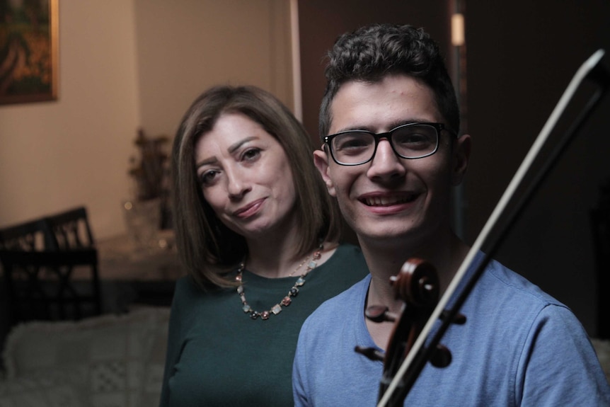 Aboud Kaplo standing with his mother Hanan and holding a violin