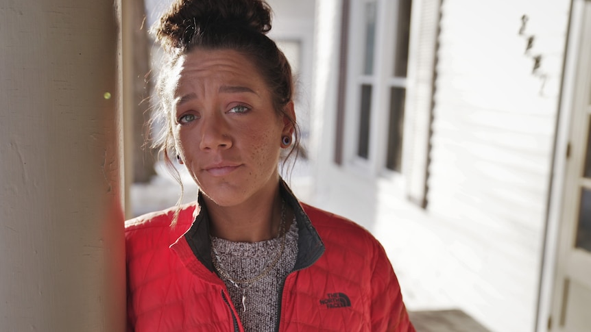 Woman standing on a porch wearing a red jacket with her hair in a bun.