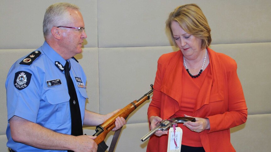 Police Commissioner Dawson holds a WW2 German rifle while talking to Minister Roberts who is holding a replica handgun.
