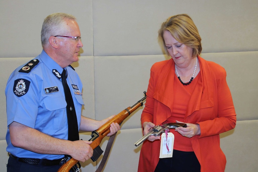 Police Commissioner Dawson holds a WW2 German rifle while talking to Minister Roberts who is holding a replica handgun.