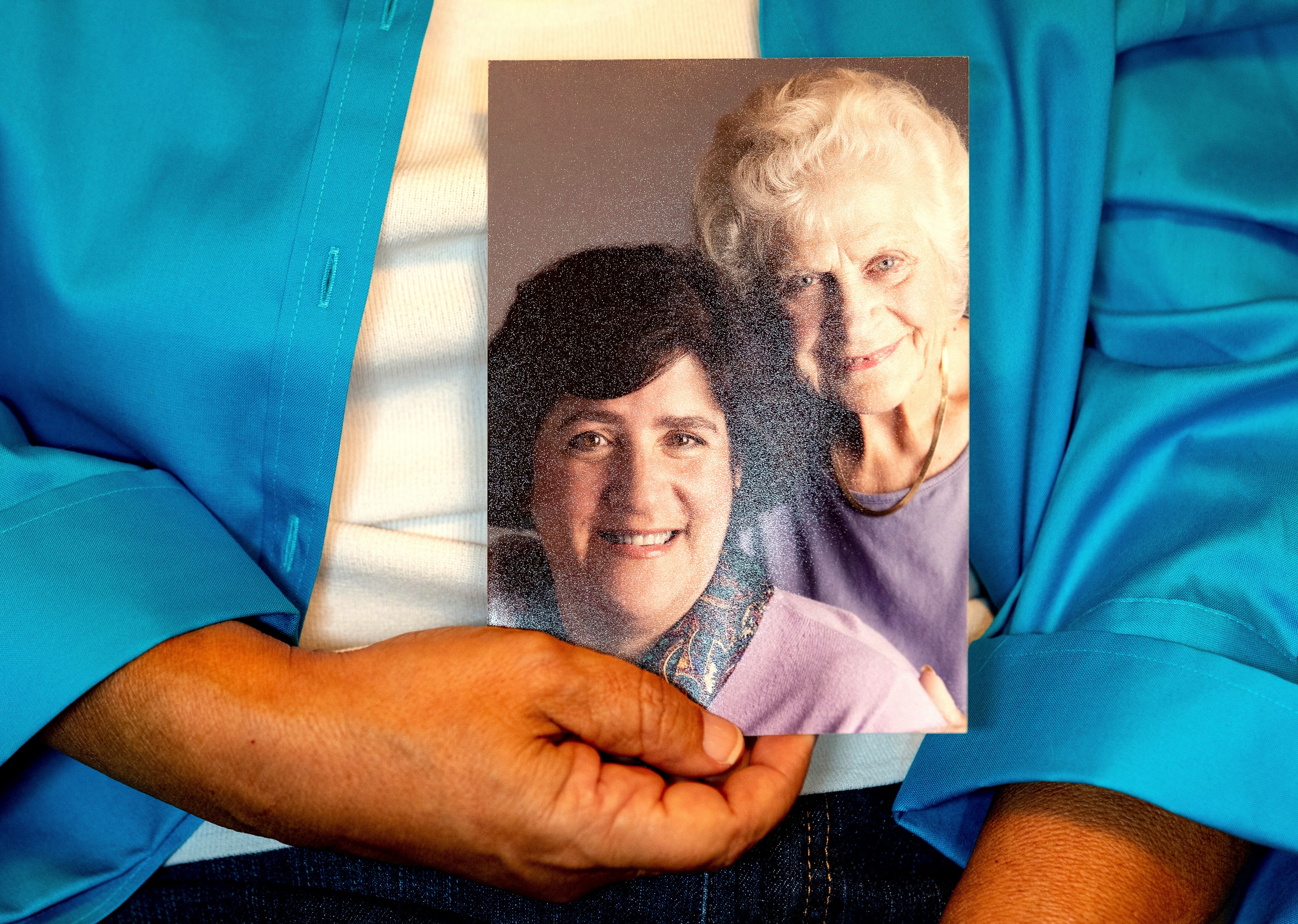 A close up of a hand holding a photo of two women smiling. One is younger with brown hair, the older with white.