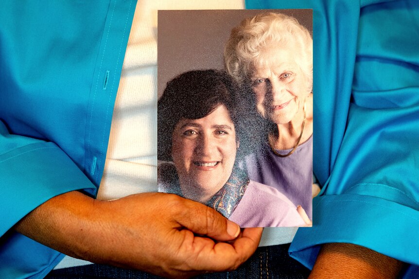 A close up of a hand holding a photo of two women smiling. One is younger with brown hair, the older with white.