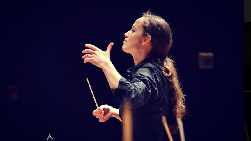 Jessica holds a baton. Instrument bows are visible in the foreground.