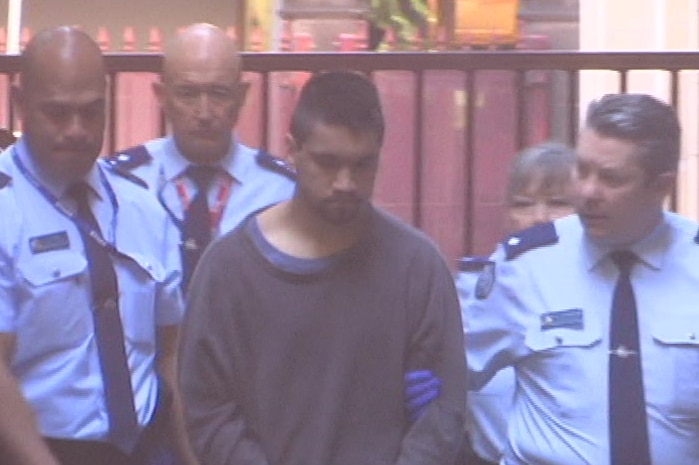 Codey Herrmann, wearing a dark blue jumper, is escorted into court by a group of corrections officials, wearing blue uniforms.