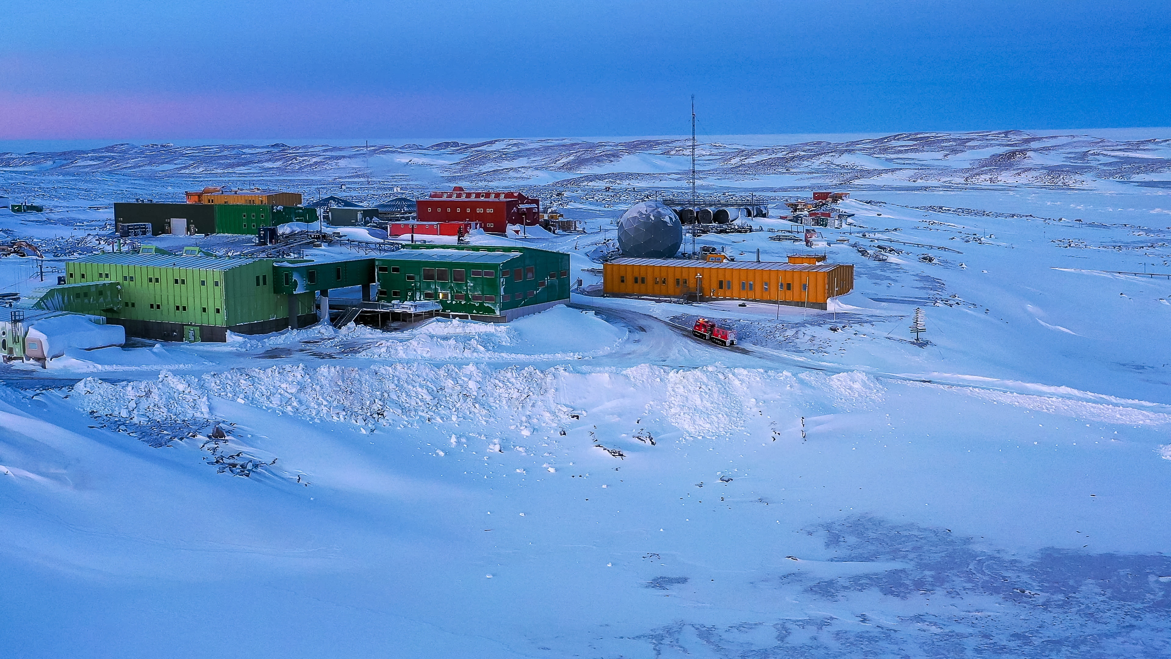 Several small buildings in snowy terrain in Antarctica.