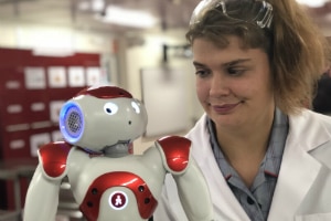 Female student in lab coat with robot.