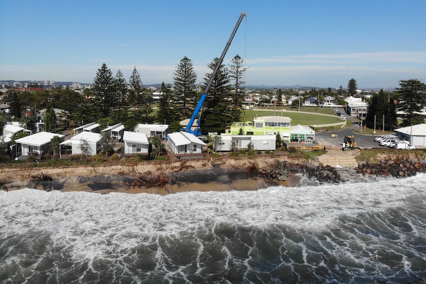 looking from a drone over the water towards the beach cabins sitti just centimetres away from the the edge of an eroded beach.