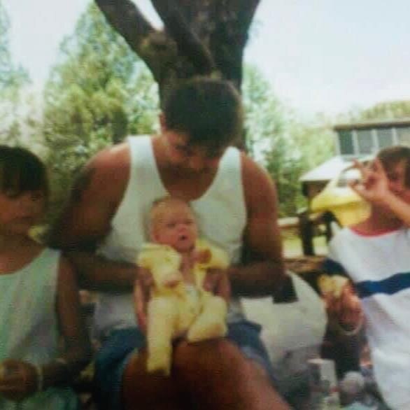 Man holding a baby with a small girl sitting to his right.