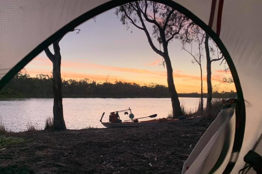 Looking out through a tent to see a kayak on the bank of the river at dusk.