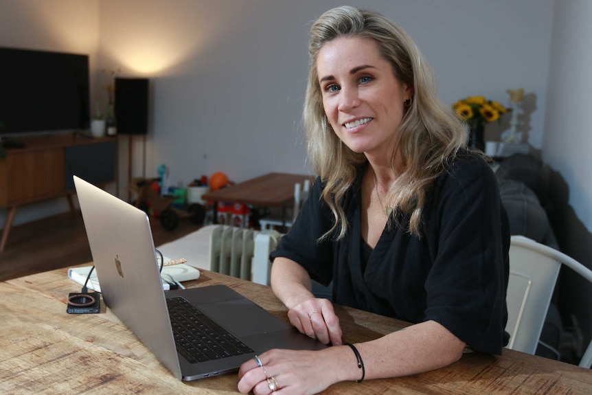 Dee Behan sits at a table with a laptop.