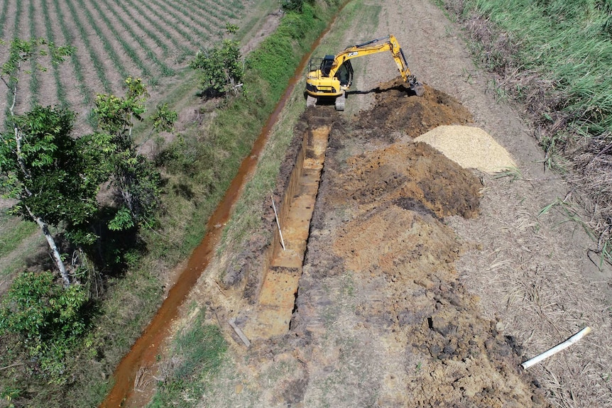 Birds eye view of a mechanical digger carving out a trench in a rural paddock.