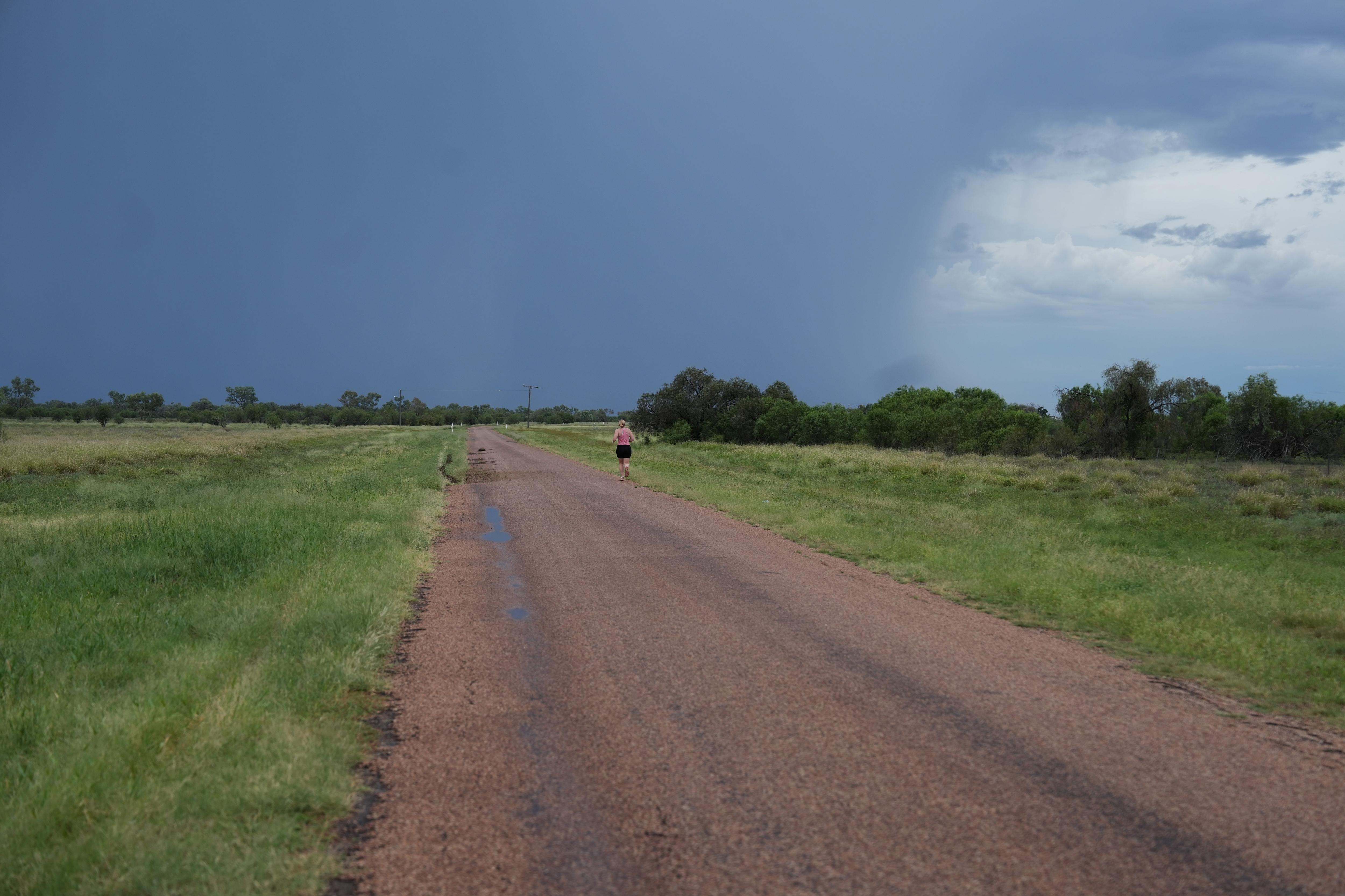 Una mujer joven en un camino rural con oscuras nubes de tormenta reuniéndose frente a ella. 