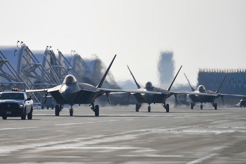Three US F-22 fighter jets taxi along a runway after landing.