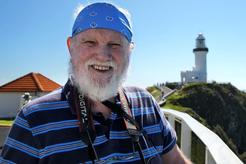 A man with a white beard and blue headscarf with a lighthouse in the background.