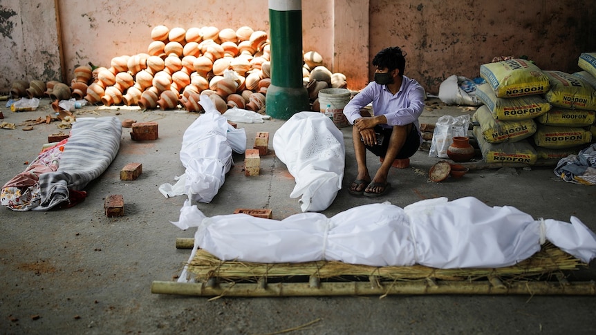 A man sits next to the bodies of those who died ahead of a mass cremation.
