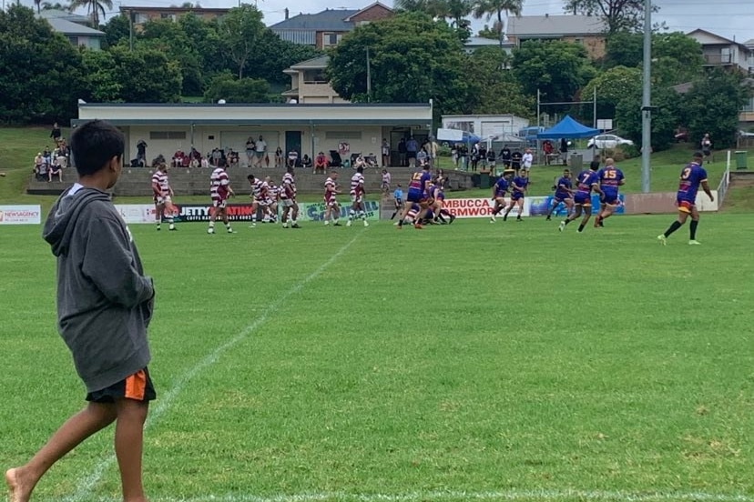 Un garçon de balle regarde deux équipes de la ligue de rugby s'affronter sur le terrain