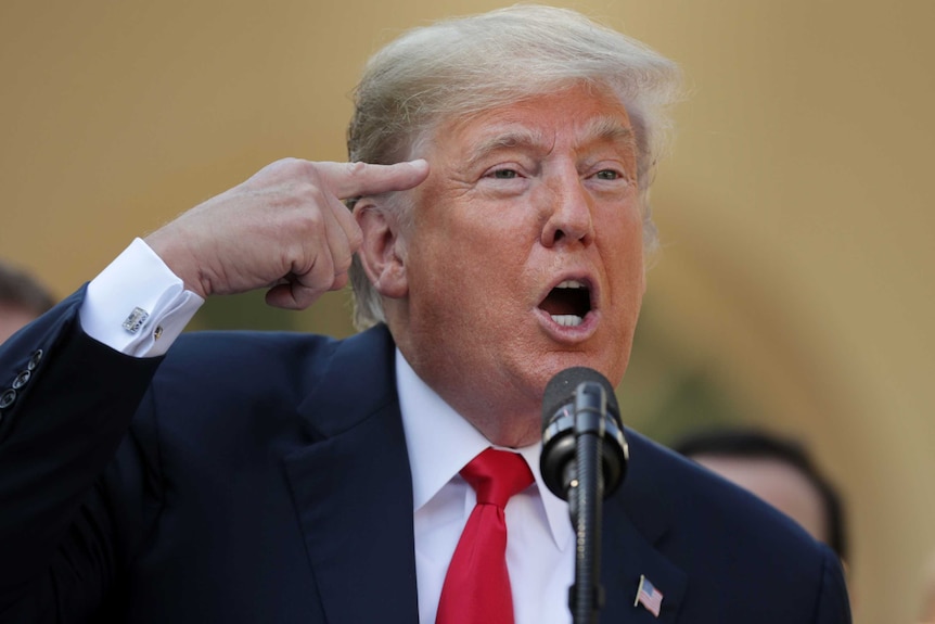 US President Donald Trump putting a finger to his head, while saying the journalists are 'loco' (crazy) in a microphone.