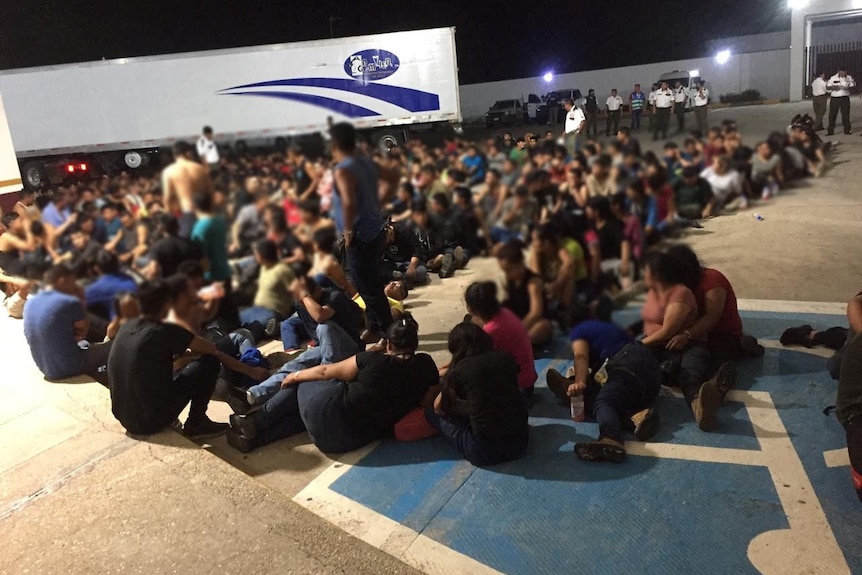 Migrants are pictured outside an abandoned truck trailer where Mexican authorities found 343 migrants from Central America.