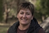 A woman with a warm vest smiles at the camera while standing in a campground.