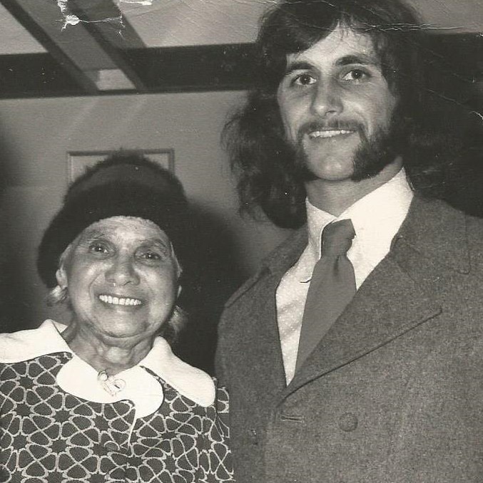 Black and white portrait of an elderly but spritely Aboriginal woman and her son with long hair and wide side burns both smiling