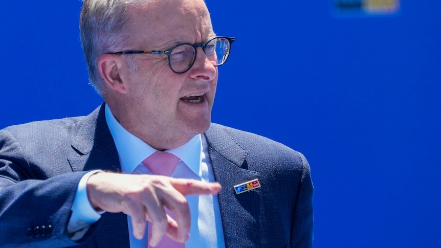 Australian Prime Minister Anthony Albanese, wearing suit and tie, gestures with his hand as he stands in front of a backdrop