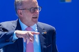 Australian Prime Minister Anthony Albanese, wearing suit and tie, gestures with his hand as he stands in front of a backdrop