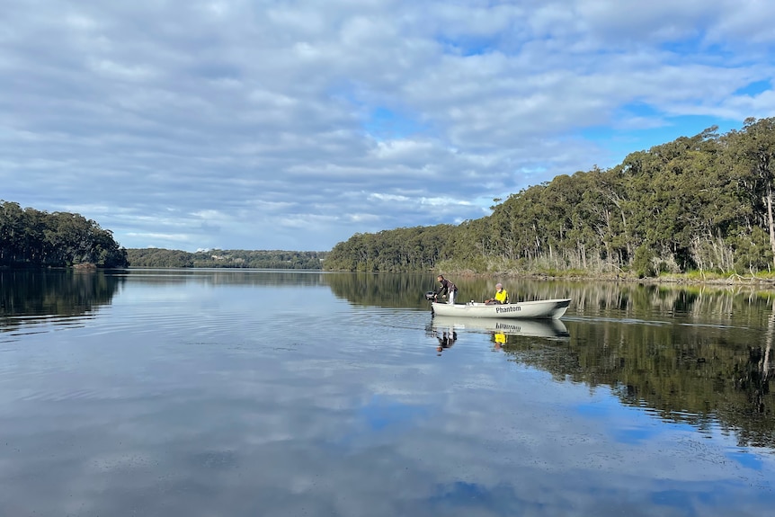 Kevin can be seen on a fishing boat in the distance, in a large body of water surrounded by trees.