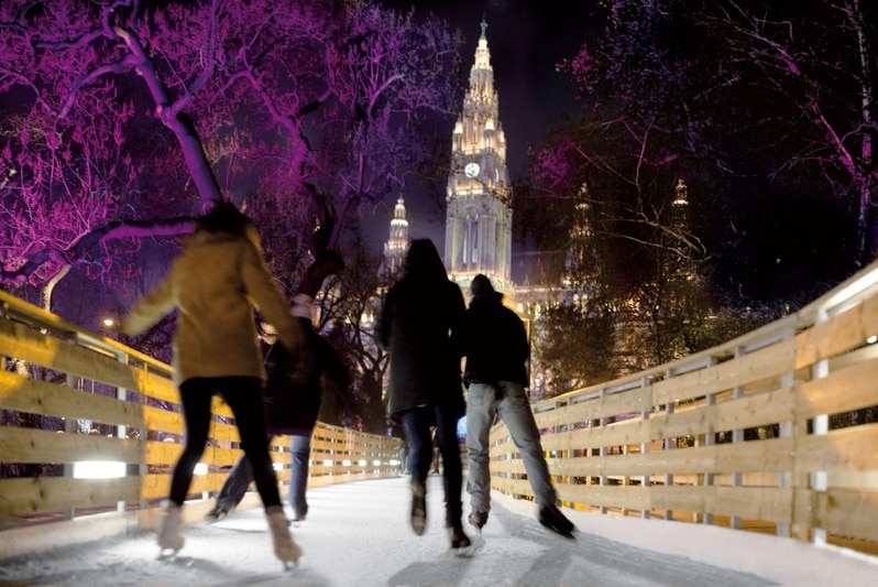 People ice skating at night at a rink in Vienna, Austria.