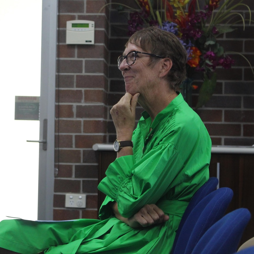A middle aged woman in a green dress smiled sitting down watching a presentation about her family history