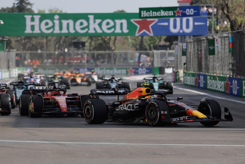 Sergio Perez leading an F1 race, turning his car into a corner as the rest of the field follows him.
