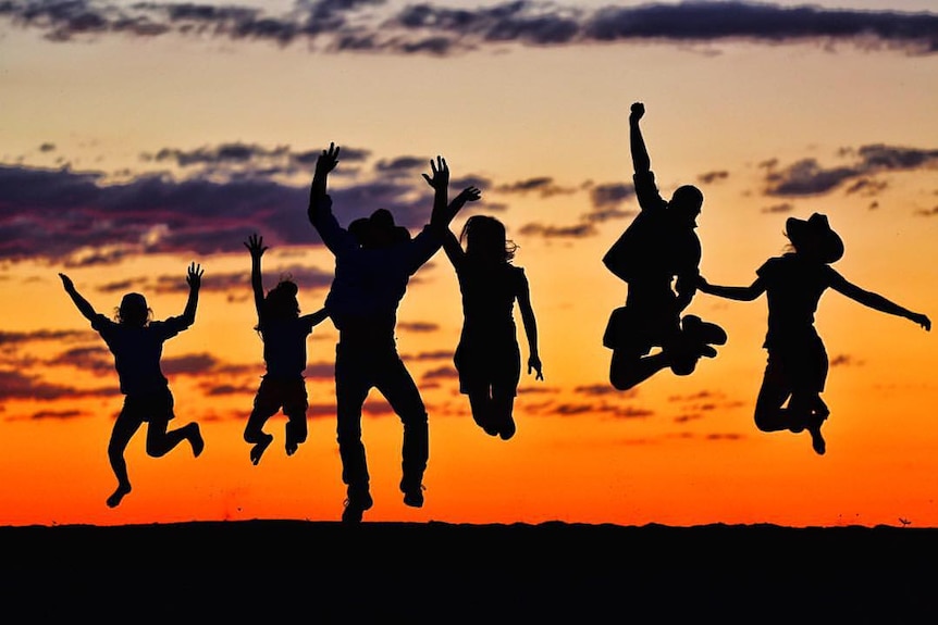 Six silhouetted figures against a sunset jump into the air.