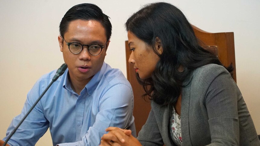 A man speaks to a woman in an Indonesian courtroom.