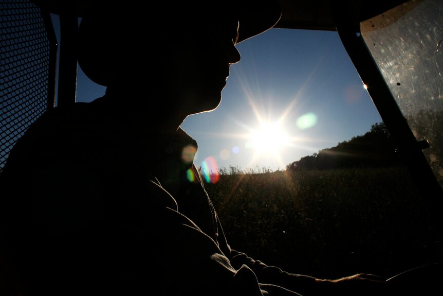A silhouette of a farmer in the cabin of a tractor.