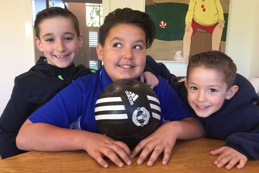 Three brothers smile for the camera as one holds a soccer ball