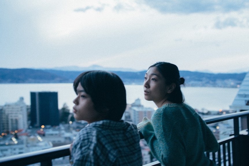 Two people look over a high-rise balcony.