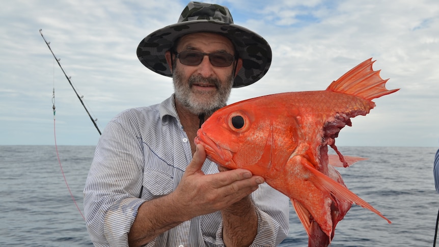 A man holds the head of a fish and smiles on a boat