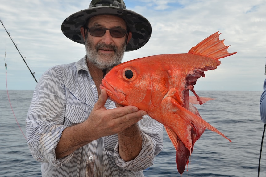 A man holds the head of a fish and smiles on a boat