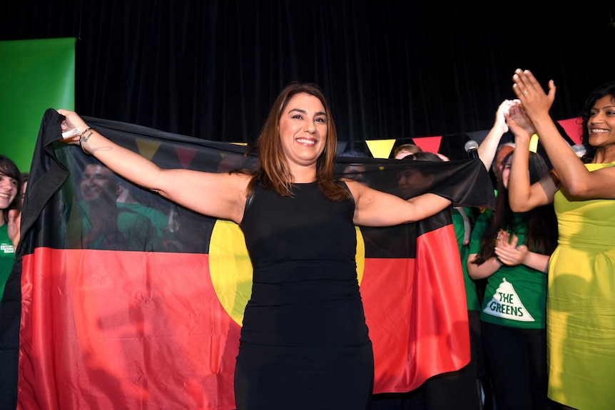 Lidia Thorpe holds an Aboriginal flag as she celebrates with supporters at a Victorian Greens function.